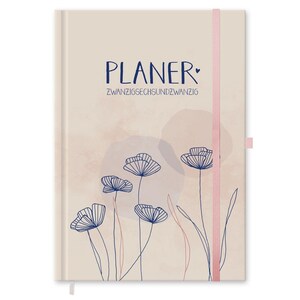 Peut inclure: Un agenda beige avec le mot "PLANER" en écriture bleu marine et le texte "ZWANZIGSECHSUNDZWANZIG" en dessous. La couverture présente un motif floral avec des fleurs bleues marine et une bande élastique rose.