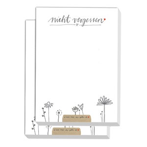 Peut inclure: Un bloc de feuilles adhésives blanches avec un motif floral noir et gris et le texte "nicht vergessen" en cursive noire avec un cœur rouge.