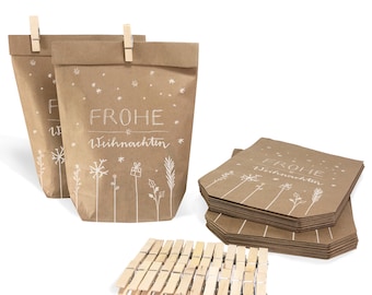 May include: Kraft paper gift bags with white snowflake and floral designs, and the words "FROHE Weihnachten". The bags are clipped closed with wooden clothespins. A stack of matching paper tags and a pile of clothespins are also visible.