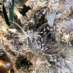 May include: Clear acrylic Christmas ornaments with white script. One is oval-shaped with the text "you don't have to get to". The other is donut-shaped with the text "NEVER EASY, ALWAYS WORTH IT, CLAD, T UP NO EXCUSES, LACEANDBELLE".