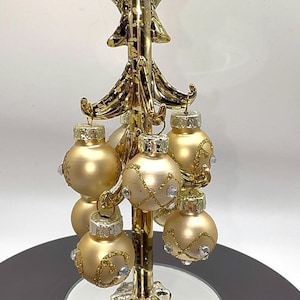 以下が含まれることがあります： 金色のクリスマスツリーの飾りで、てっぺんに星が付いています。ツリーには、キラキラとクリスタルのアクセントが付いた、いくつかの金のオーナメントがあります。ツリーは鏡張りのベースにあります。