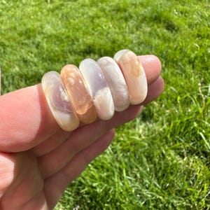 May include: Five rings made of pink and white agate, stacked on top of each other. The rings are smooth and polished.
