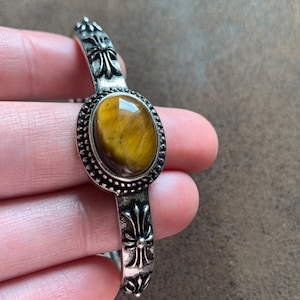 May include: A silver bracelet with a tiger's eye stone and a cross design.