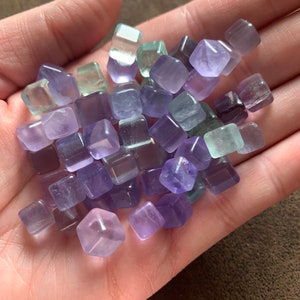 May include: A collection of small, purple and green fluorite cubes. The cubes are translucent and have a variety of shades of purple and green.