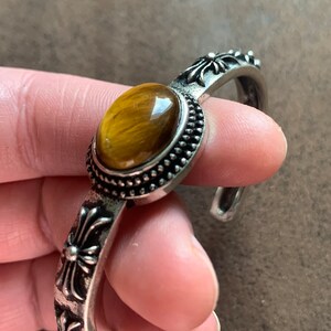May include: Silver bracelet with a tiger's eye stone and cross accents.