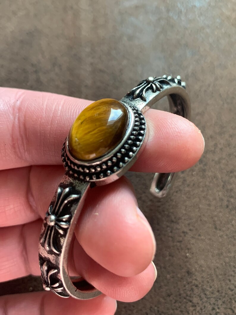 May include: Silver bracelet with a tiger's eye stone and cross accents.