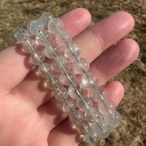 May include: A bracelet made of clear, faceted, round beads with a slight green tint. The beads are strung on a silver wire.