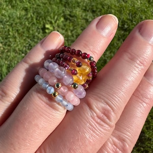 May include: A stack of colorful beaded rings, including pink, purple, blue, yellow, and red beads. The rings are worn on a finger.