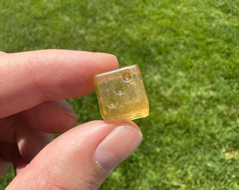 May include: A clear yellow gummy candy shaped like a cube with rounded edges. The candy has a translucent appearance and appears to have air bubbles inside.