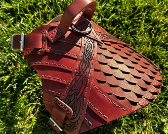 May include: A brown leather dog harness with a Celtic knot design and a silver buckle. The harness has a scale-like pattern and is designed for a medium-sized dog.