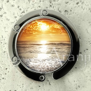 May include: A silver metal key chain with a round image of a sunset over the ocean. The image is in a circular frame with a silver metal border.