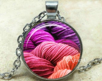 May include: A silver chain necklace with a round pendant featuring a close-up image of pink, purple, and orange yarn.