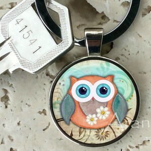 May include: A silver key chain with a round, colorful owl charm. The owl is orange with blue eyes and a turquoise and white patterned design. The key chain has a silver key with the number 41541 on it.