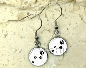 May include: A pair of silver earrings with white round charms featuring black paw prints.