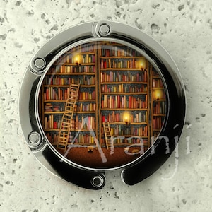 May include: A silver-toned, round, folding bag charm with a picture of a bookshelf filled with books and lit by candles. The bookshelf has two ladders.