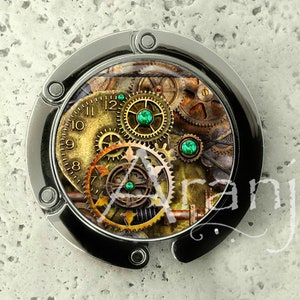 May include: A silver-toned metal bag clip with a round, clear plastic insert featuring a steampunk design. The design includes a clock face, gears, and green gemstones.