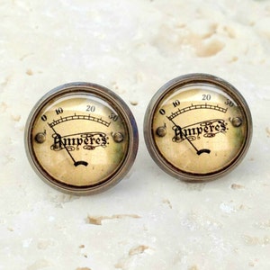 May include: A pair of gold-toned earrings with a vintage-style amp meter design. The earrings feature a round face with a black needle and the word "Amperes" printed in black.