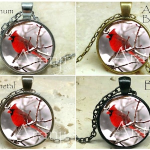 May include: A necklace with a round pendant featuring a red cardinal perched on a snowy branch. The pendant is available in platinum, antique bronze, gunmetal, and black.