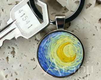 May include: A silver keychain with a round, blue, yellow, and white enamel charm featuring a painting of a starry night sky with a crescent moon. The charm is attached to a silver ring and a black key ring.