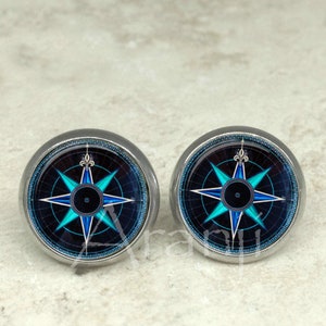 May include: A pair of silver stud earrings with a compass design. The compass features a blue and white star on a black background.