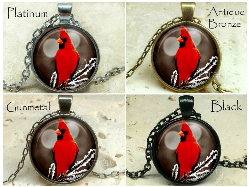 May include: A necklace with a round glass pendant featuring a red cardinal perched on a snowy branch. The pendant is available in four different metal finishes: platinum, antique bronze, gunmetal, and black.
