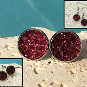 May include: A pair of silver stud earrings with a red glitter design. The earrings are round and have a smooth, polished finish.