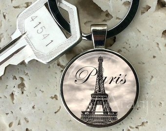 May include: A silver keychain with a black and white photo of the Eiffel Tower in Paris. The photo is in a round, silver frame. The keychain also has a silver key with the number 41541 engraved on it.