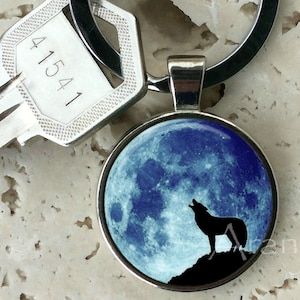 May include: A silver key chain with a round, blue and white glass charm featuring a silhouette of a wolf howling at the full moon.
