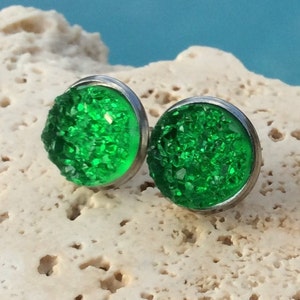 May include: A pair of green glass stud earrings with a silver setting. The earrings are round and have a sparkly, textured surface.