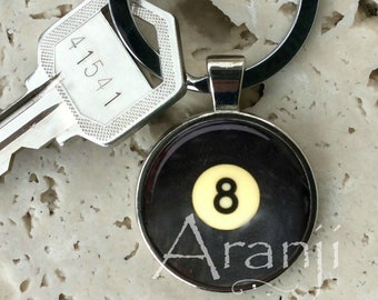 May include: A silver keychain with a black and white 8-ball charm. The charm has the number 8 in white on a yellow background. The text "Aranji" is printed on the charm.