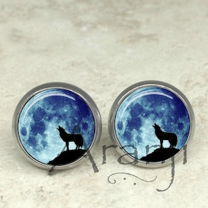 May include: A pair of silver stud earrings with a blue moon and a black silhouette of a wolf howling at the moon.