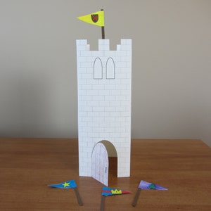 May include: A white paper castle with a yellow flag with a red cross on top. There are three flags on the ground, one blue with a yellow star, one yellow with a red crown, and one blue with a green tree.