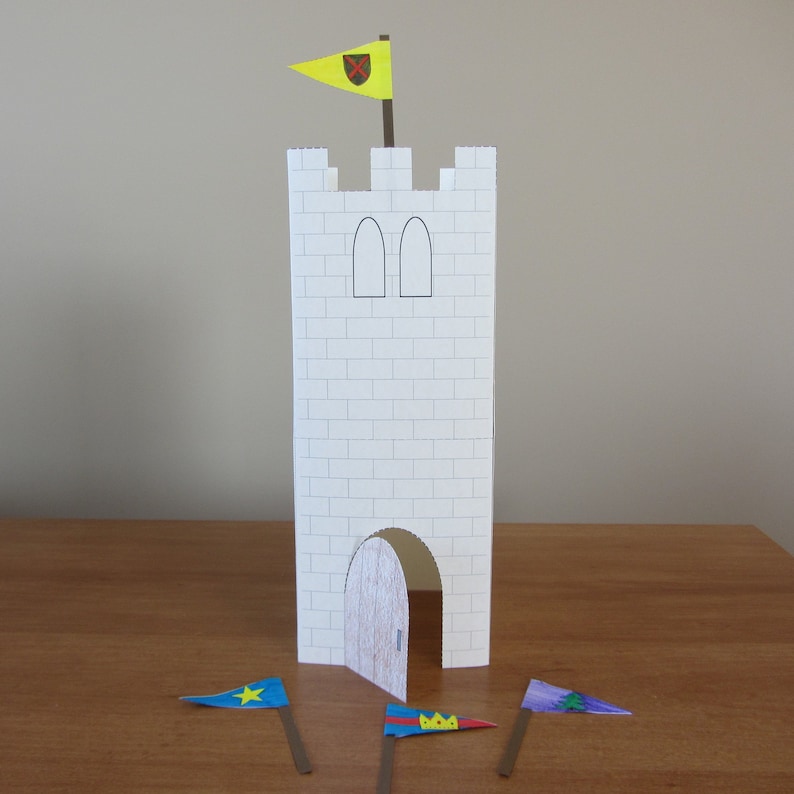 May include: A white paper castle with a yellow flag with a red cross on top. There are three flags on the ground, one blue with a yellow star, one yellow with a red crown, and one blue with a green tree.