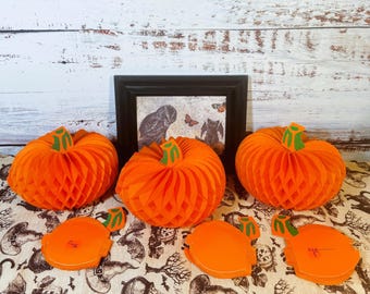 May include: Three orange paper pumpkins with a honeycomb texture. The pumpkins are on a white and brown patterned surface.