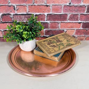 May include: A copper serving tray with a raised rim, featuring a small potted plant and two antique books stacked on top of each other. The top book has the title "The Oak & The Books" on the cover.