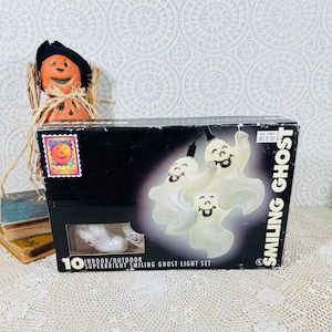 May include: A black rectangular box for a 10-count indoor/outdoor super-bright smiling ghost light set. The packaging features white text reading SMILING GHOST and displays an image of three white, illuminated ghost-shaped light covers.