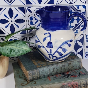 May include: A blue and white ceramic jug with a floral design. The jug is sitting on top of two vintage books.