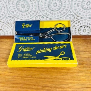May include: A set of chrome-plated pinking shears in a yellow and blue box. The box reads "Griffon" and "pinking shears". The shears are open, showing the serrated blades. The box also states "Ball Bearing, Self Adjusting, All Chrome Plated."