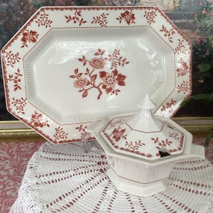 May include: White ceramic serving dish and lidded soup tureen with a red floral pattern. The serving dish is rectangular with a scalloped edge. The tureen has a matching floral design and a small spoon. A vintage style.