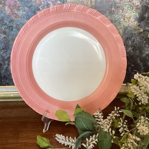 May include: A pink and white vintage dinner plate with a scalloped edge and a raised design around the rim.