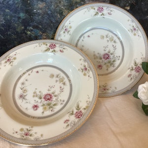 May include: Two white ceramic soup bowls with a gold rim and floral pattern. The bowls have a delicate floral design in shades of pink, green, and brown.