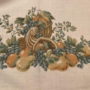 May include: A light beige fabric featuring a printed pattern of a cornucopia overflowing with various fruits including pears, oranges, and clusters of grapes, accented by green leaves and branches arranged in a horizontal decorative border.