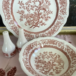 May include: A set of three white ceramic dishes with a red and white floral pattern. The dishes include a large platter, a smaller bowl, and two salt and pepper shakers.