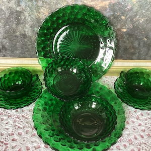 May include: A set of emerald green glass tableware featuring a raised hobnail texture. The collection includes a large plate, two smaller bowls, and two teacups with matching saucers, all displaying a consistent circular pattern and translucent finish.