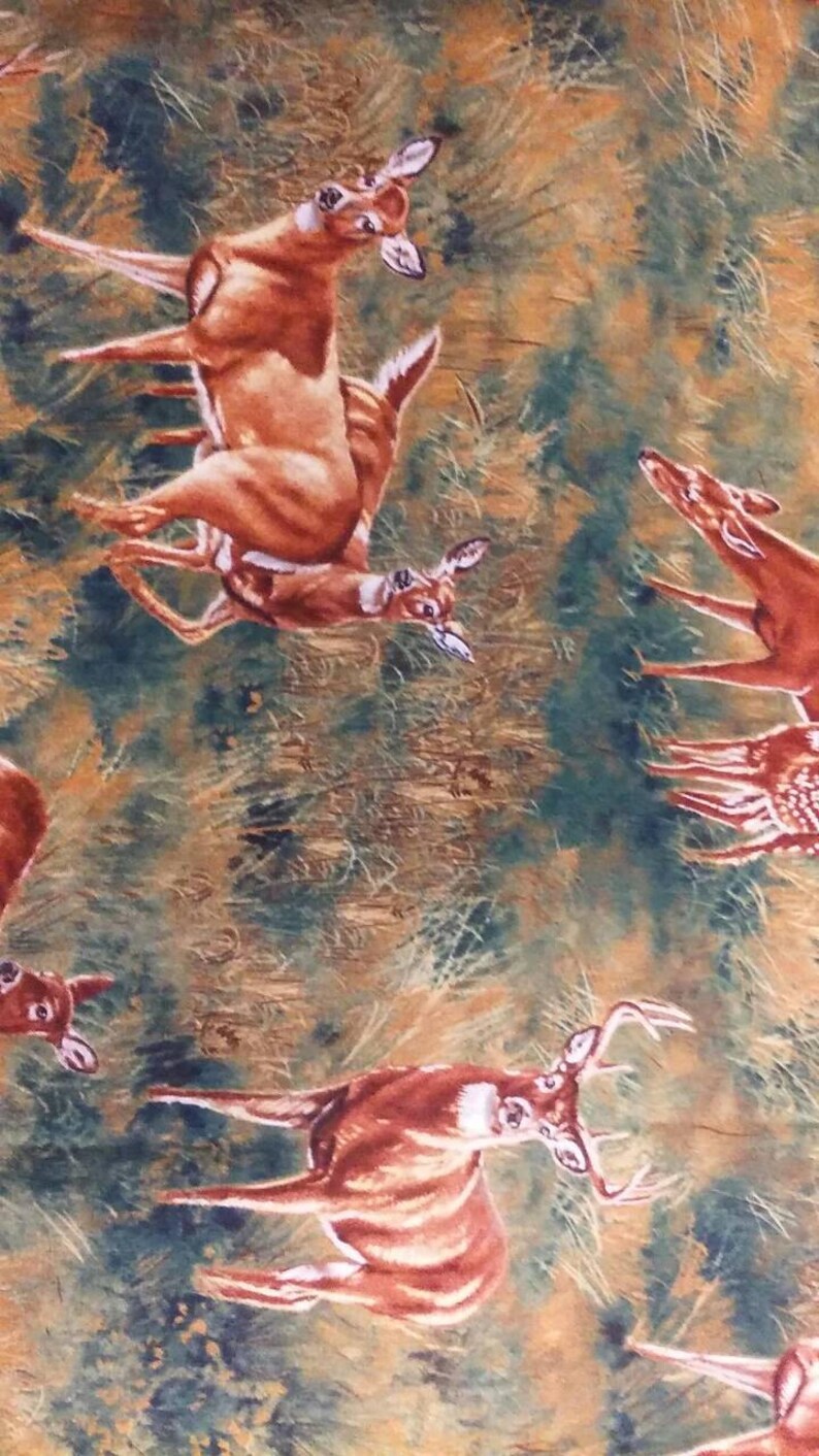 K&ouml;nnte beinhalten: Ein brauner und gr&uuml;ner Stoff mit einem sich wiederholenden Muster aus Hirschen. Die Hirsche sind in verschiedenen Posen, darunter stehend, laufend und springend. Der Stoff hat ein rustikales und waldiges Flair.