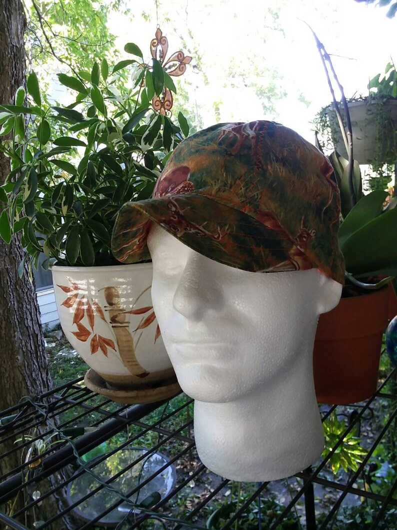 K&ouml;nnte beinhalten: Eine Baseballkappe mit einem gekr&uuml;mmten Schirm in einem Muster aus Gr&uuml;n, Braun und Orange. Die Kappe sitzt auf einem wei&szlig;en Styropor-Kopf.
