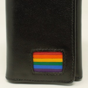 Puede incluir: Cartera de cuero negra de tres pliegues con un parche de bandera arcoíris en la parte delantera.