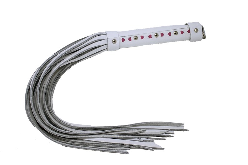 May include: White leather whip with a pink heart design and silver studs. The whip has a long handle and a fringed end.