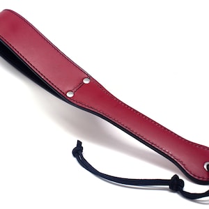 May include: A red leather paddle with a black strap and a silver ring at the end.