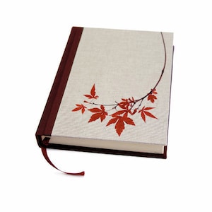 May include: A hardbound journal with a beige linen cover and a burgundy spine. The cover features a branch with red maple leaves. A burgundy ribbon bookmark is attached.